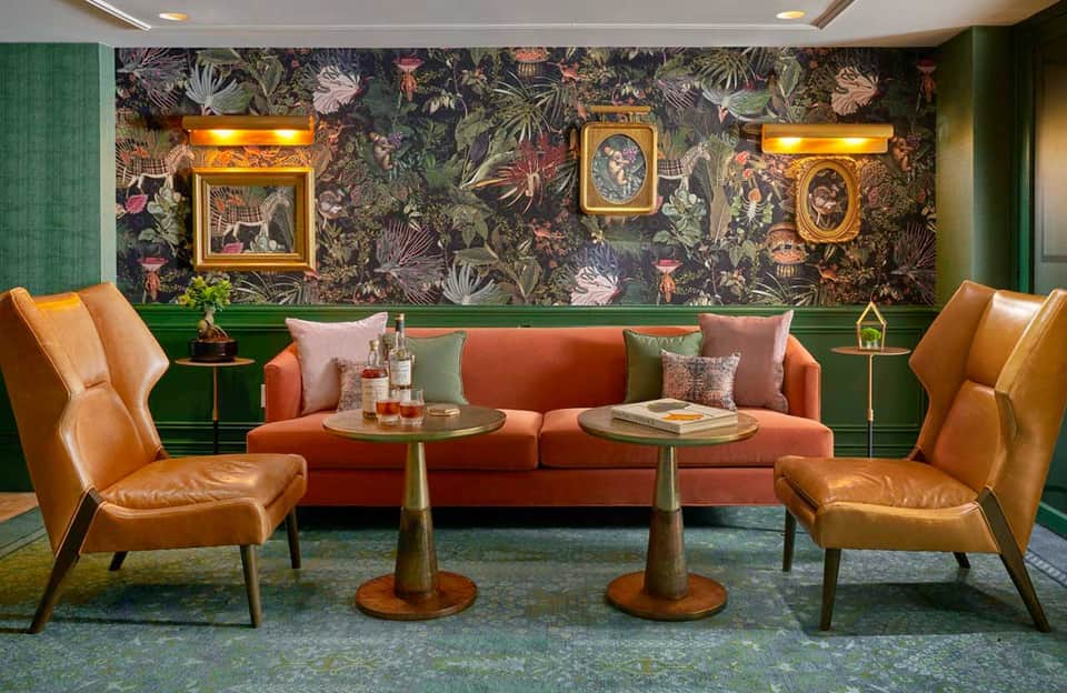 Luxury lounge with coral sofa, cognac leather chairs, botanical wallpaper, and gold-framed art