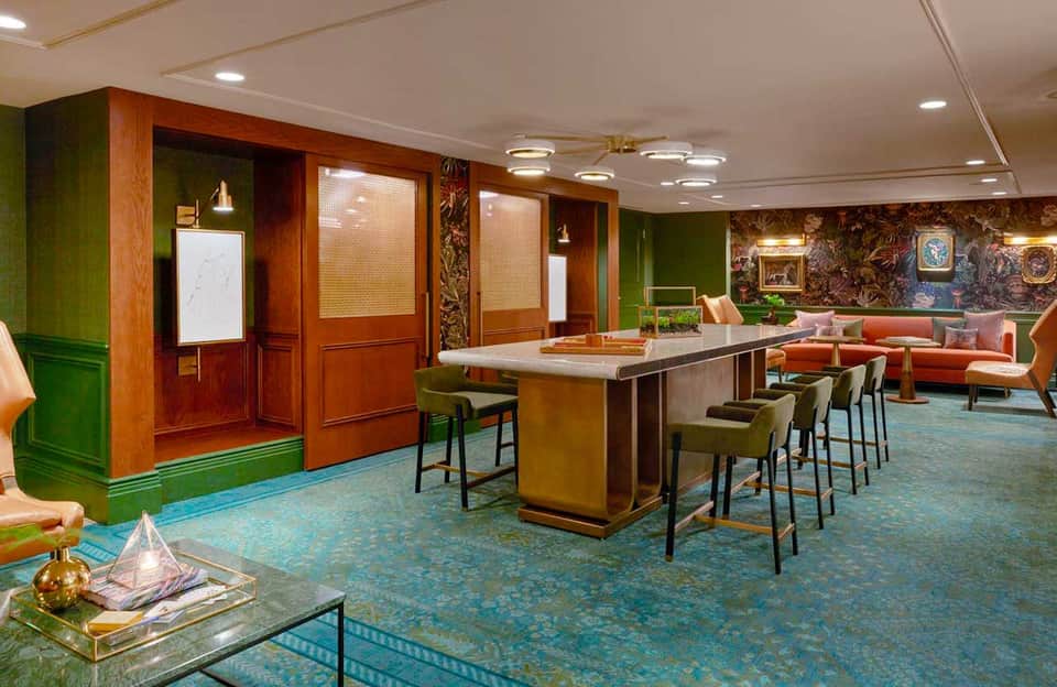 Upscale lounge with wood paneling, green walls, bar counter, colorful seating, patterned floor