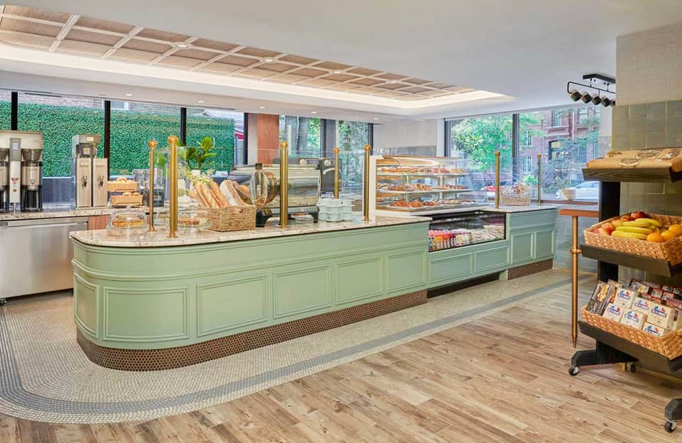Bright modern bakery interior with mint-green curved counter, bread displays, and garden wall