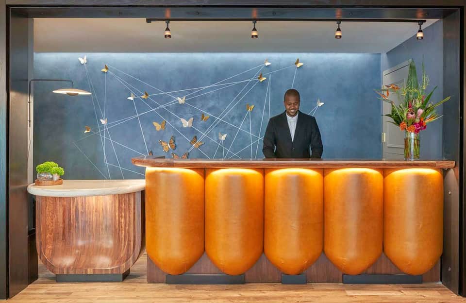 Modern hotel lobby with blue accent wall, gold cylindrical sculptural elements, and wooden reception desk