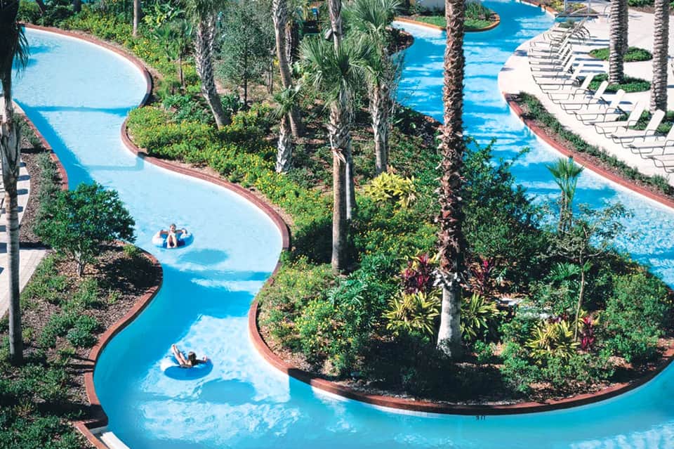 Aerial view of lazy river with turquoise water winding through lush tropical landscaping and palm trees