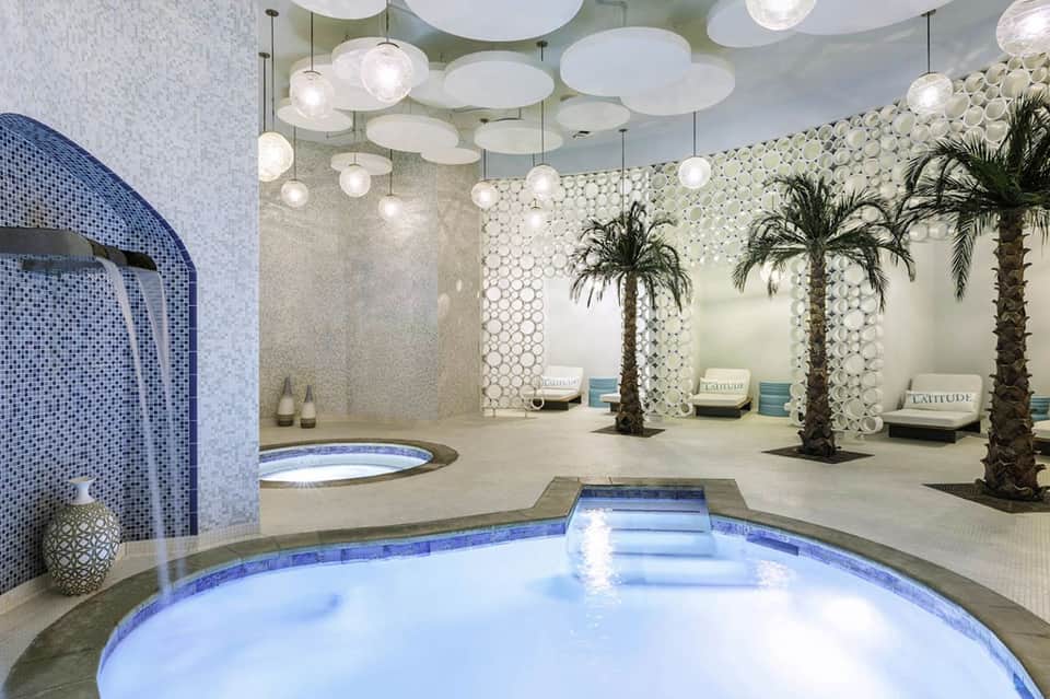 Spa interior with illuminated pools, pendant lighting, palm trees, and modern tilework