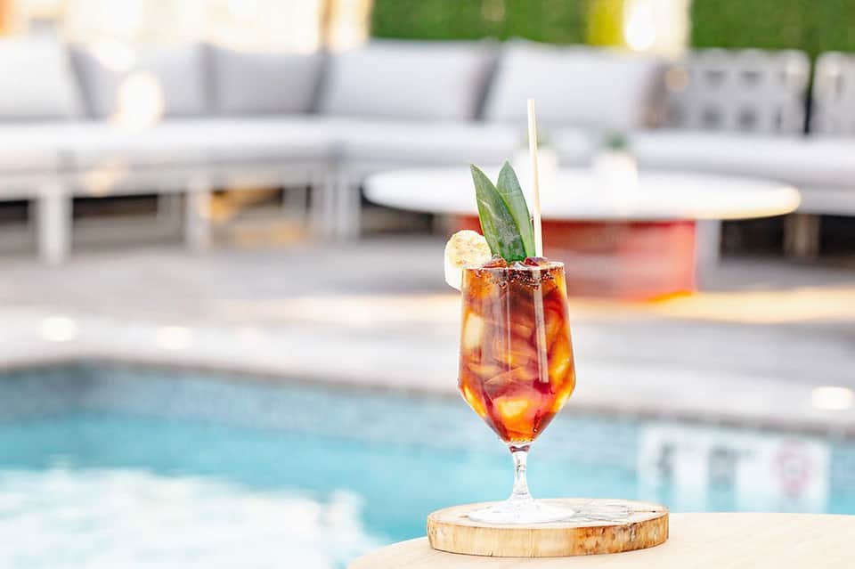 Tropical cocktail with garnish on wooden coaster by resort pool