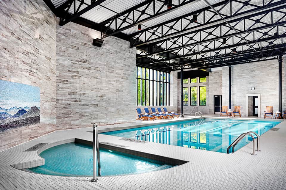 Indoor aquatic center with lap pool, hot tub, lounge chairs, and modern architectural design
