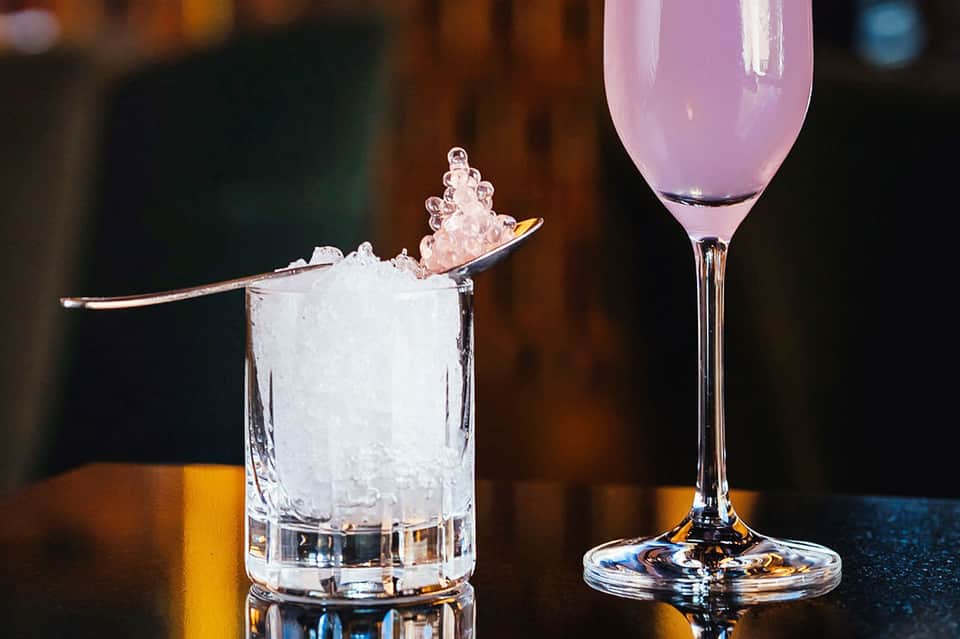 Two signature cocktails - iced drink with spoon and pink champagne cocktail on bar