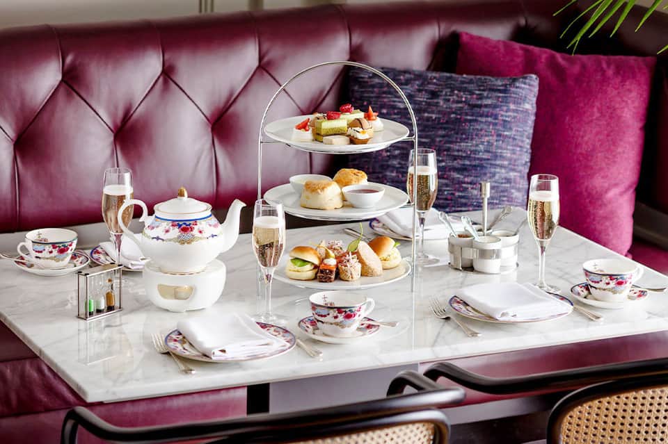 Elegant afternoon tea service with tiered stand, pastries, champagne, and magenta tufted sofa