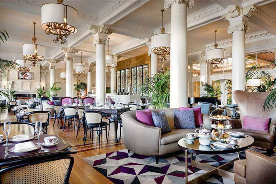 Elegant hotel lobby with white columns, ornate chandeliers, and purple accent chairs