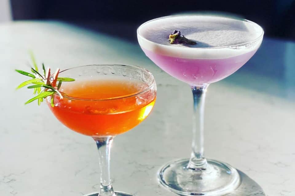 Two artisanal cocktails with garnishes on a marble surface against ocean backdrop