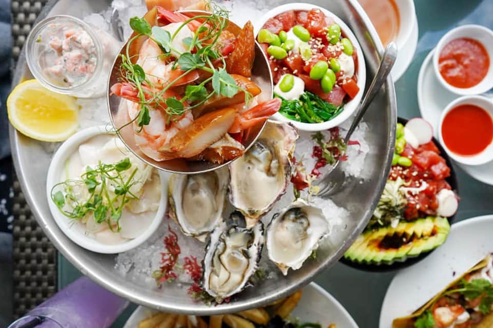 Overhead view of fresh seafood platter with oysters, shrimp, and colorful garnishes on ice