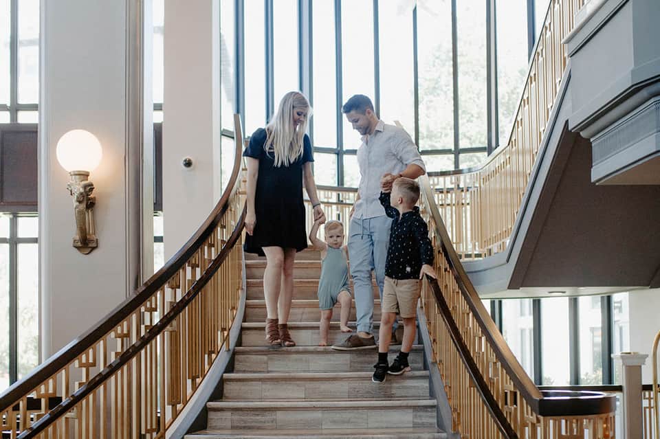 Family of four descending modern staircase with natural light and wooden railings in contemporary hotel lobby