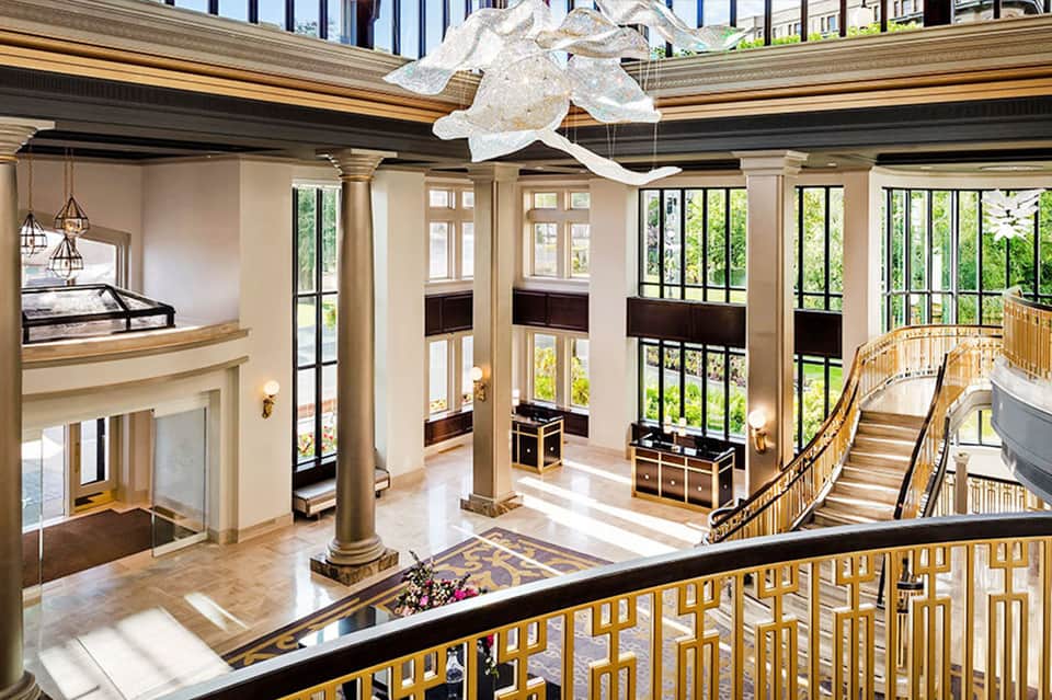 Grand hotel lobby with double staircase, high ceilings, columns, and natural light from large windows