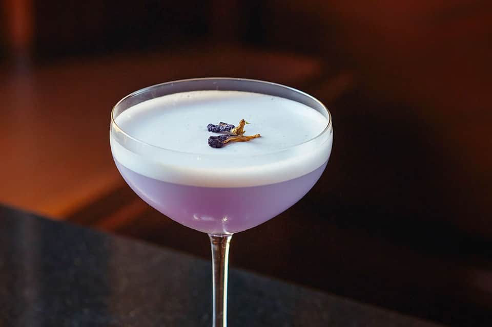 Elegant cocktail with lavender color and white foam topped with dried flower garnish