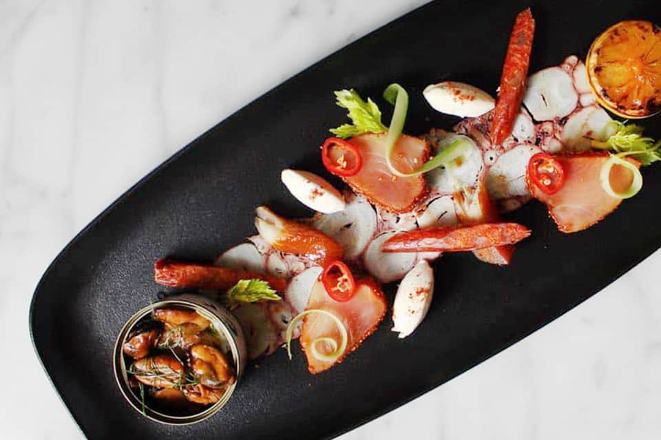 Grilled seafood platter with lobster, shrimp, clams, and garnish on black slate