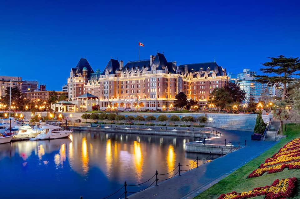 Illuminated historic castle-style hotel reflected in calm water at dusk with landscaped grounds