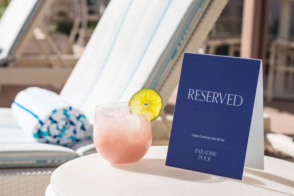 Poolside cocktail with lemon garnish next to a blue 'Reserved' sign at Paradise Pool