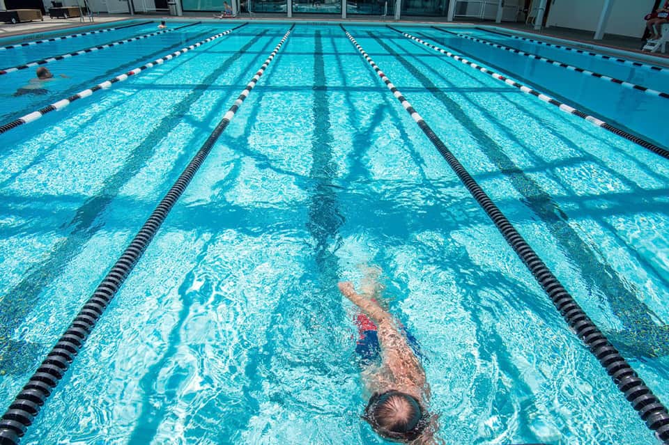 Olympic-size swimming pool with lane dividers and a swimmer doing freestyle stroke
