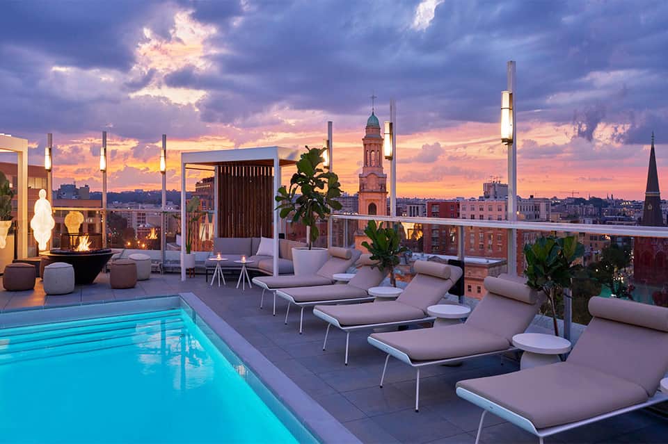 Rooftop pool at sunset with city skyline view, lounge chairs, and illuminated architectural elements