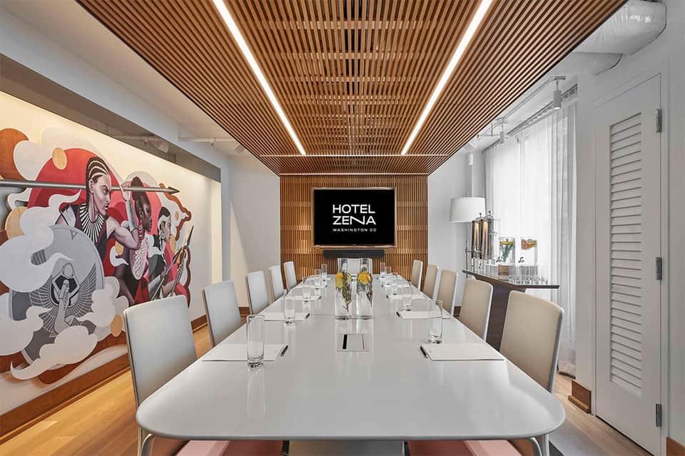 Modern hotel conference room with long white table, wooden ceiling, and video display