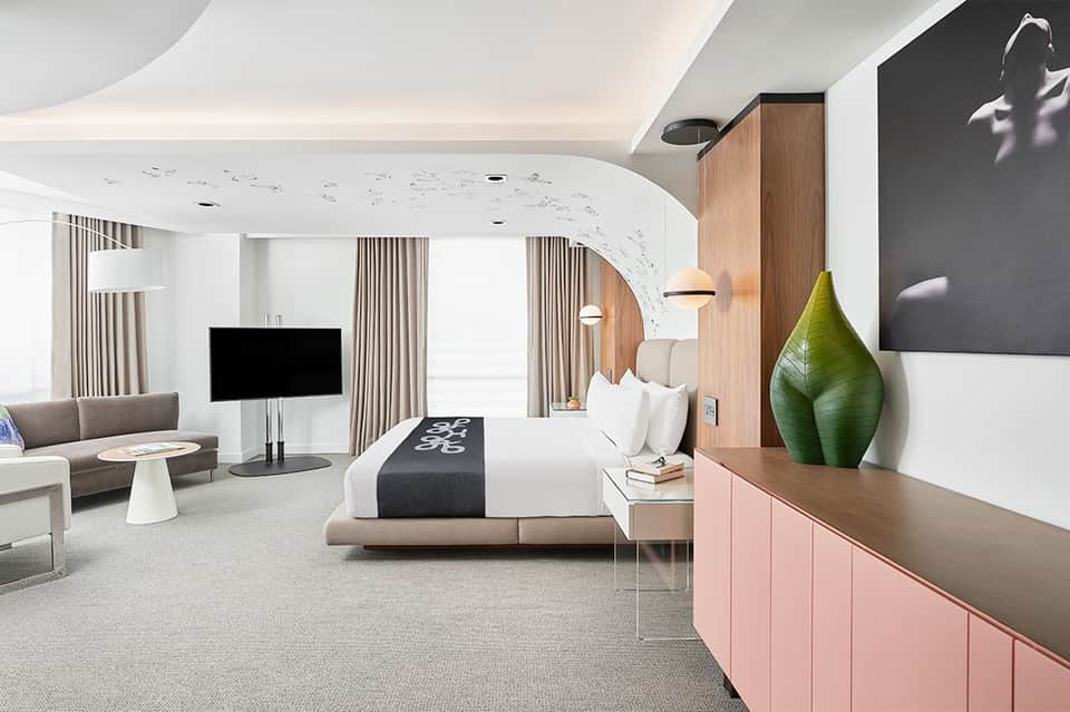 Modern hotel suite with curved white ceiling, bed, living area, wood accents, and contemporary furnishings