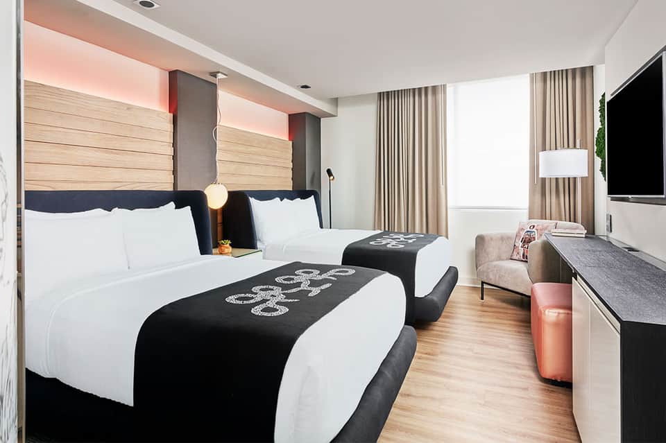 Modern hotel room with two queen beds, wooden headboards, black accents, and contemporary furnishings