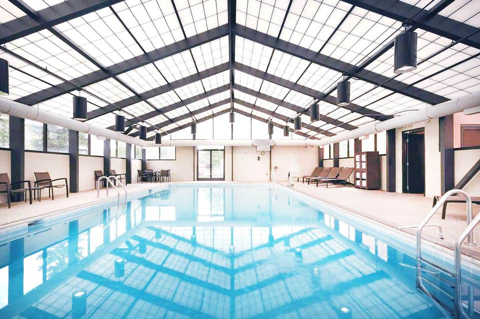 Indoor lap pool with skylighting, lounge chairs, and accessible deck space in modern facility