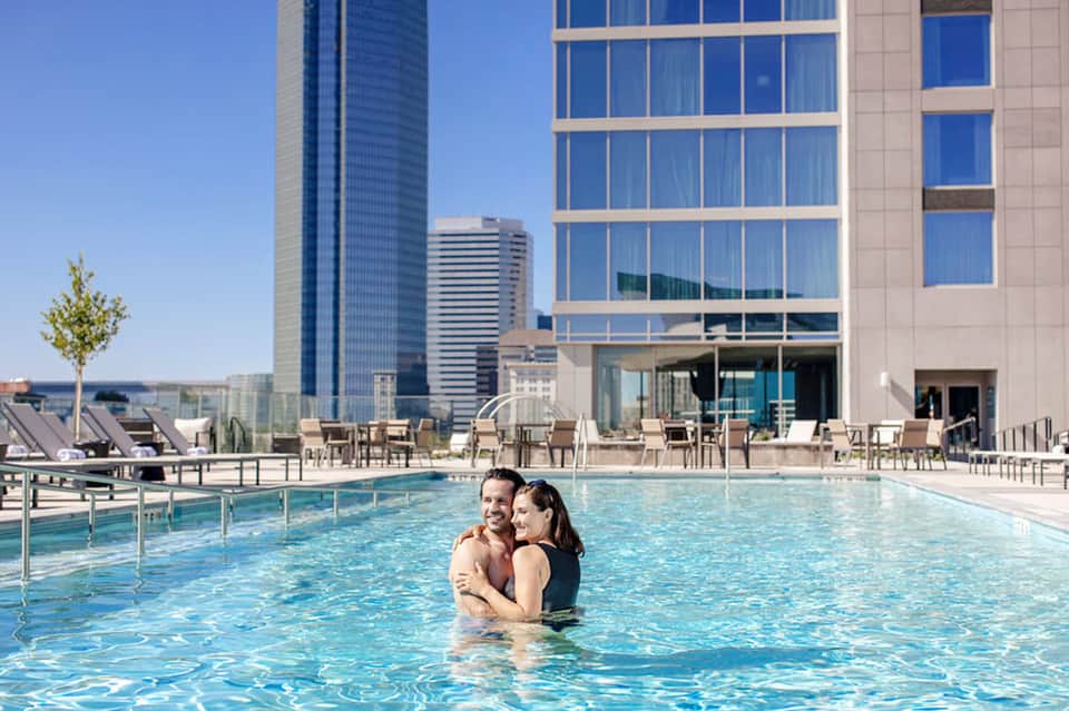 Family swimming in a modern rooftop pool with downtown city skyline and tall buildings in background
