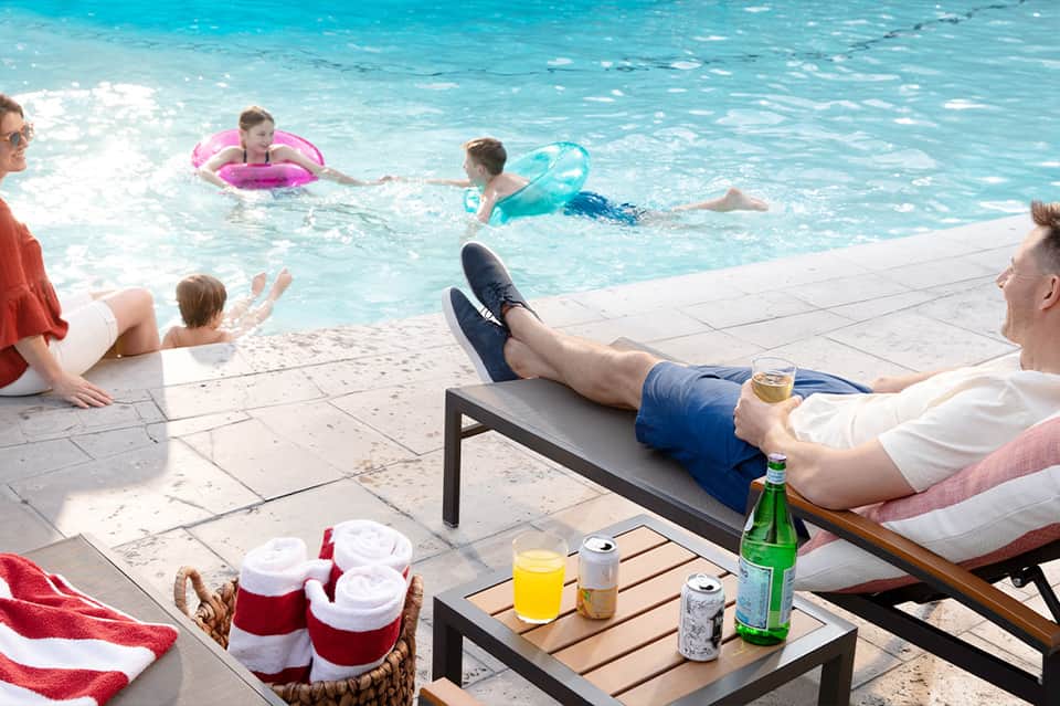 Family enjoying tropical resort beach with turquoise water, lounge chairs, and refreshments on the deck.