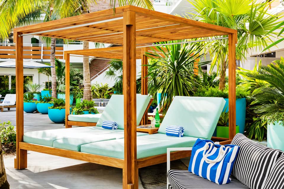 Wooden canopy daybed with white cushions surrounded by tropical plants in resort courtyard