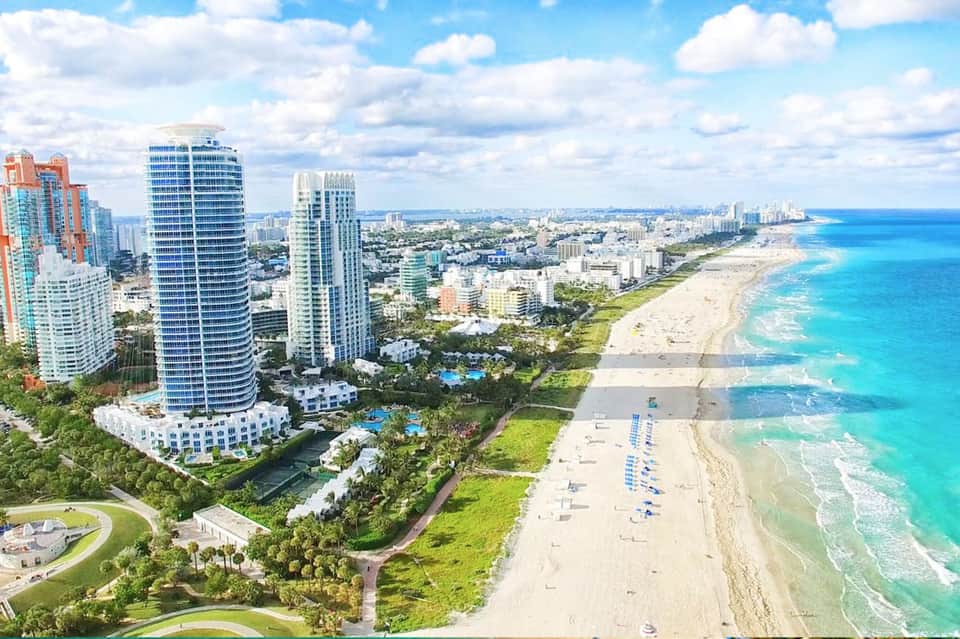 Aerial view of beachfront high-rise resort with sandy beach, turquoise ocean, and tropical landscaping
