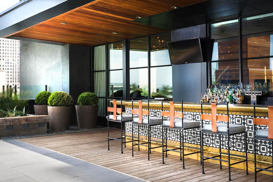Modern resort patio with wooden ceiling, lounge chairs, geometric patterned seating, and garden views