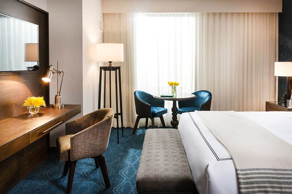 Modern hotel room with king bed, work desk, seating area, and ocean view curtains