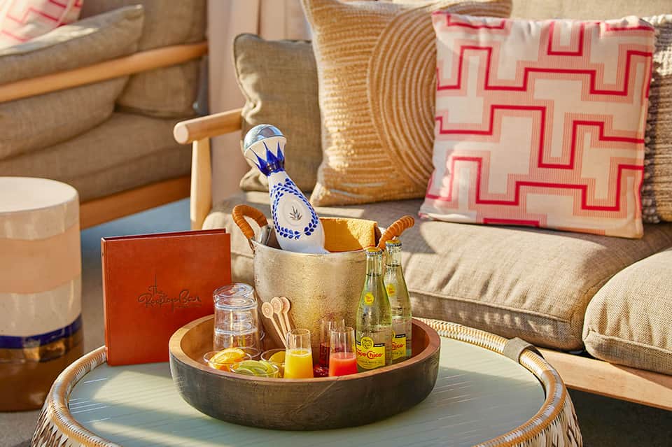 Elegant living room detail with decorative pillows, woven side table, and styled coffee table with beverages