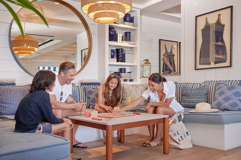 Family playing board games on a striped sofa in a nautical-themed resort lounge with modern decor