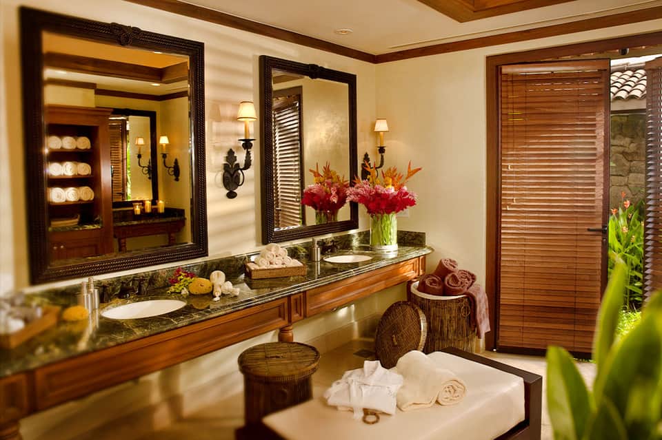 Luxury bathroom with dual vanities, ornate mirrors, tropical flowers, and wooden details