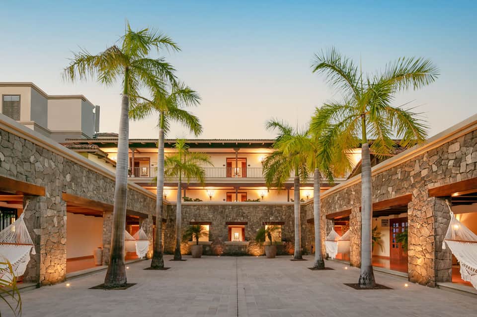 Tropical courtyard with palm trees, stone archways, and terracotta-roofed buildings at dusk