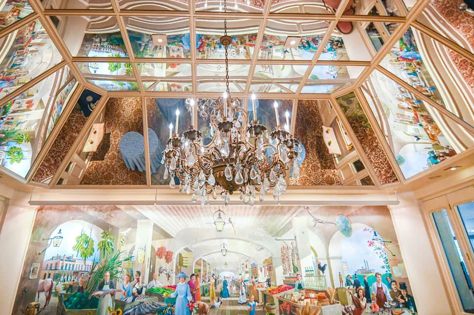 Elegant glass-ceiling corridor with chandelier and colorful marketplace mural artwork