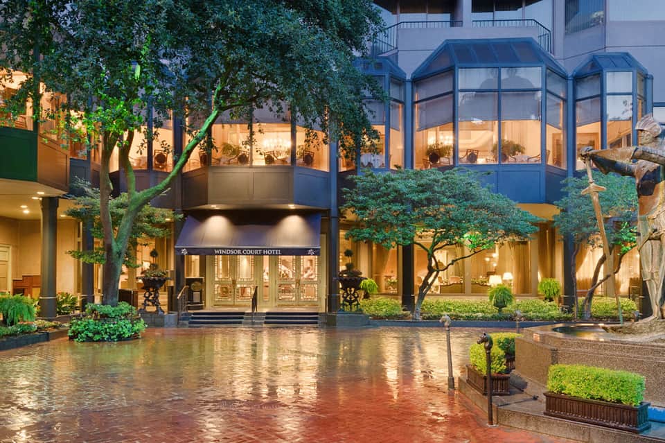 Windsor Court Hotel entrance with elegant courtyard, mature trees, and illuminated storefront at dusk