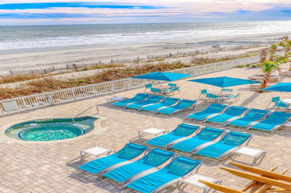 Beachfront resort deck with blue lounge chairs, umbrellas, and ocean view