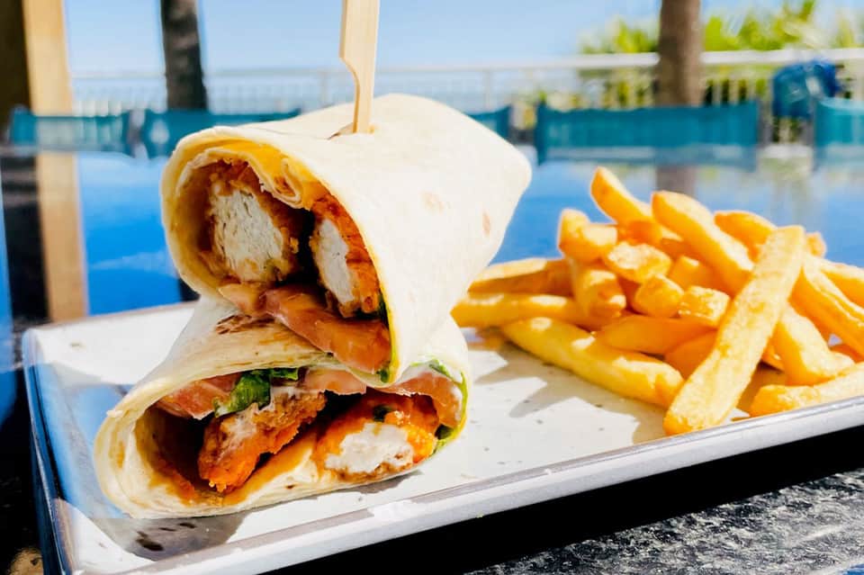 Wrapped chicken shawarma and French fries on a plate by a poolside.