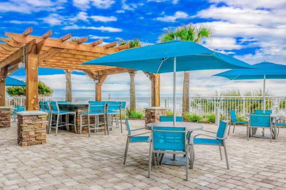 Oceanview terrace with turquoise umbrellas, wooden pergola, and coastal blue water views