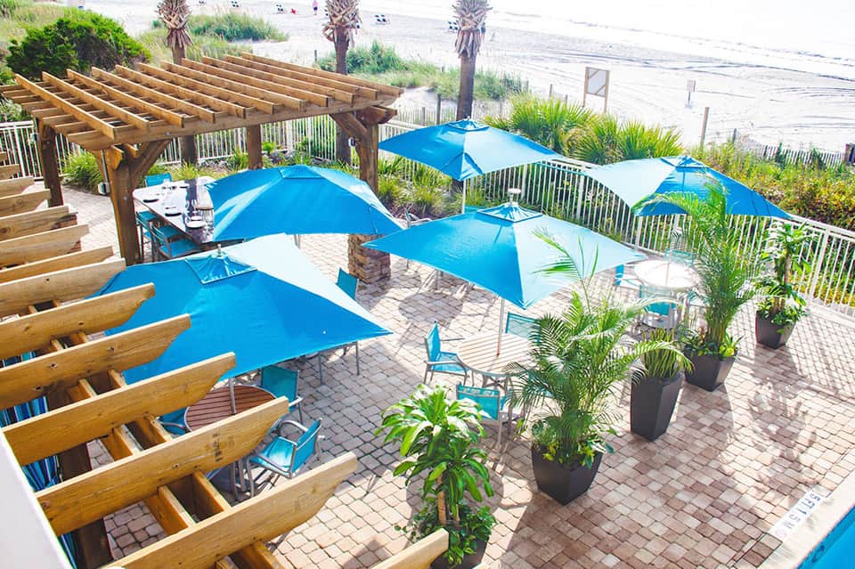 Beachfront deck with blue umbrellas, wooden pergola, and ocean views