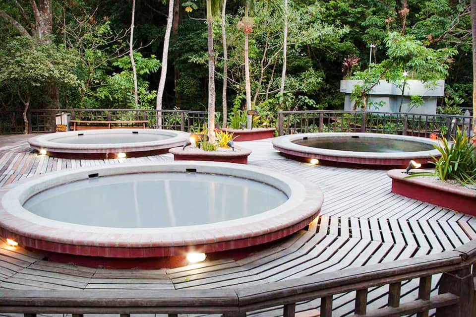 Outdoor spa area with three circular hot tubs on wooden deck surrounded by lush forest landscape