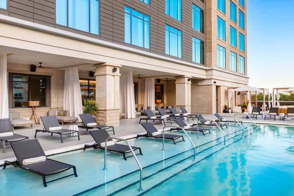Contemporary hotel indoor pool with lounge chairs, modern building architecture, and covered cabanas