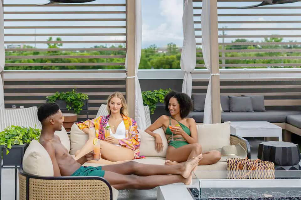 Three guests relaxing on modern rooftop lounge furniture with horizontal slat privacy screens and greenery