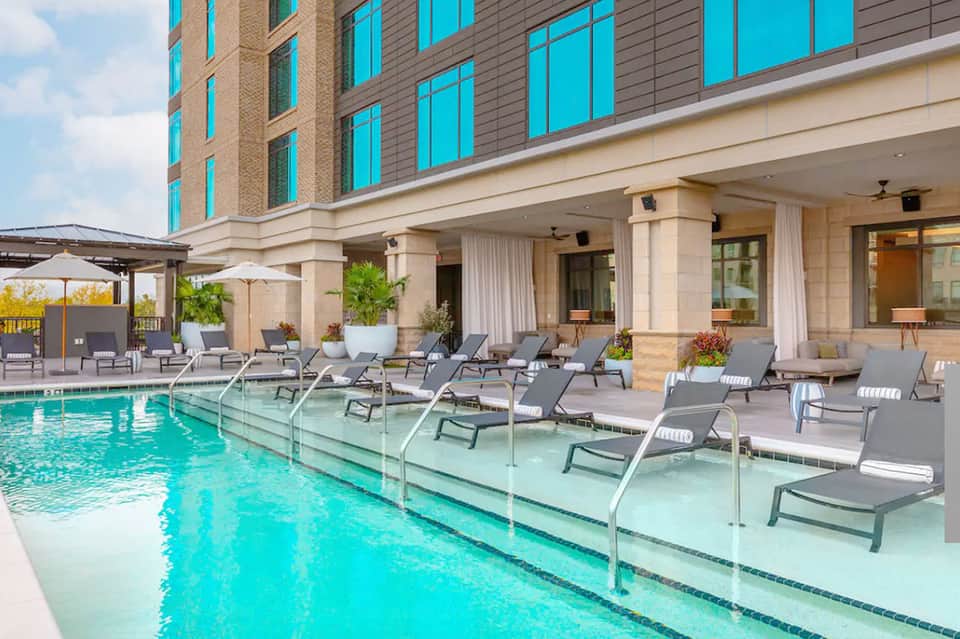 Contemporary hotel pool with glass railing, lounge chairs, and modern building facade with turquoise windows