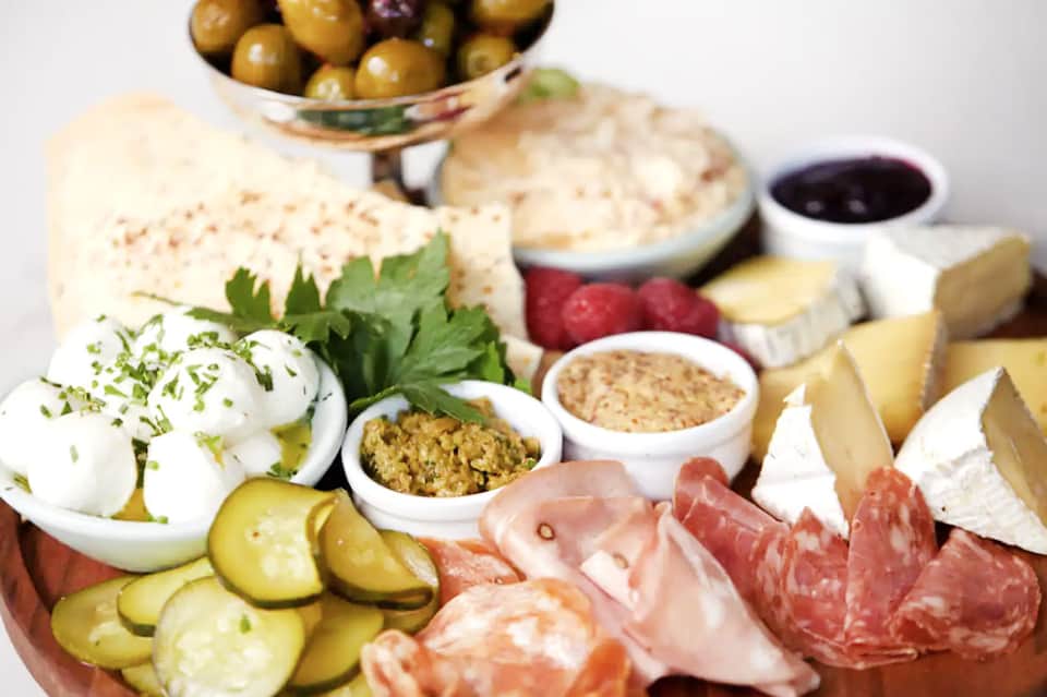 Gourmet charcuterie and cheese board with olives, cured meats, crackers, pickles, and condiments