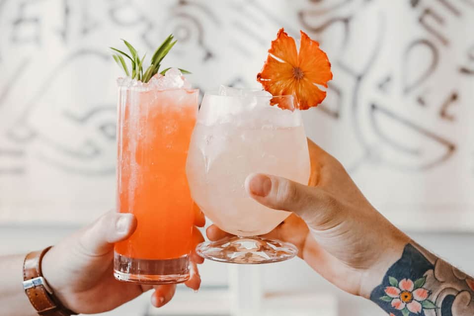 Two colorful tropical cocktails with citrus garnishes held by two hands