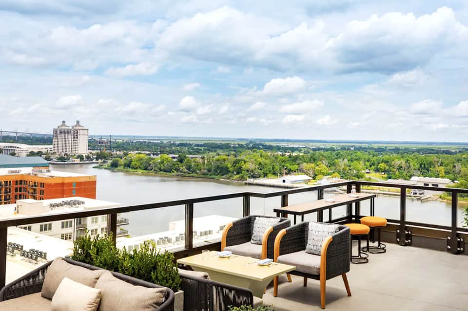 Rooftop terrace with lounge seating overlooking a river and distant landscape under cloudy sky