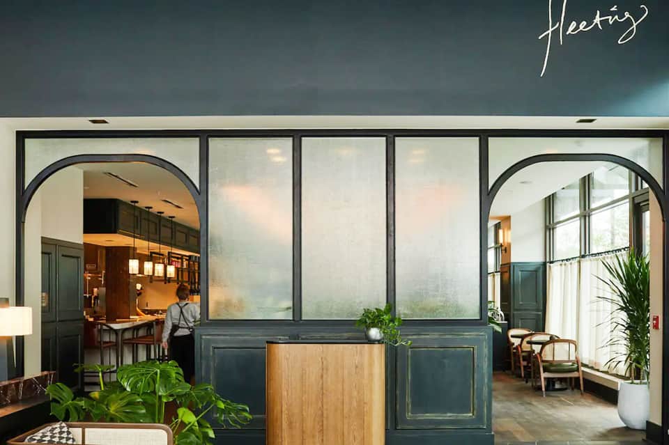 Elegant hotel entrance with dark teal paneling, arched glass doorways, white walls, and potted plants.