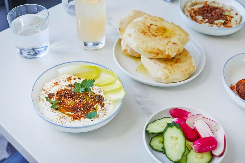 Mediterranean breakfast spread with hummus, pita bread, fresh vegetables, and beverages